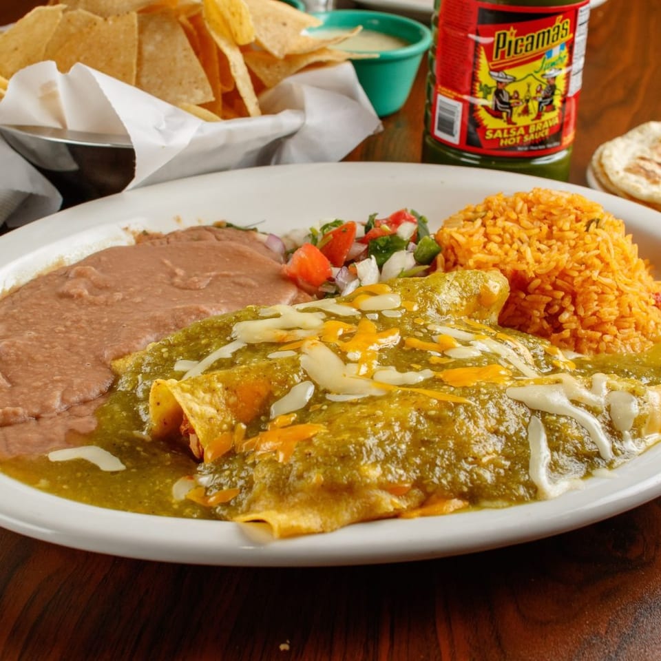 A plate of green enchiladas with rice, refried beans, pico de gallo, chips, and hot sauce.