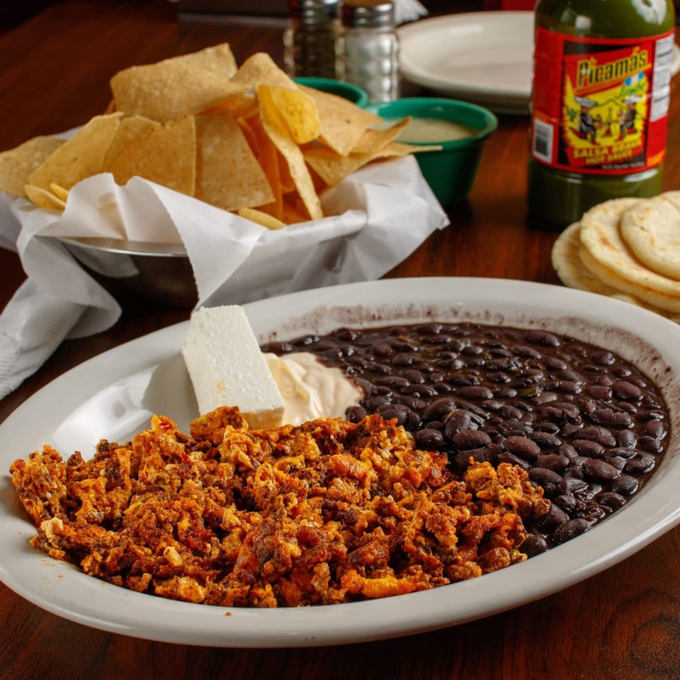 A plate of scrambled eggs with chorizo, black beans, cheese, and sour cream, with chips and tortillas.