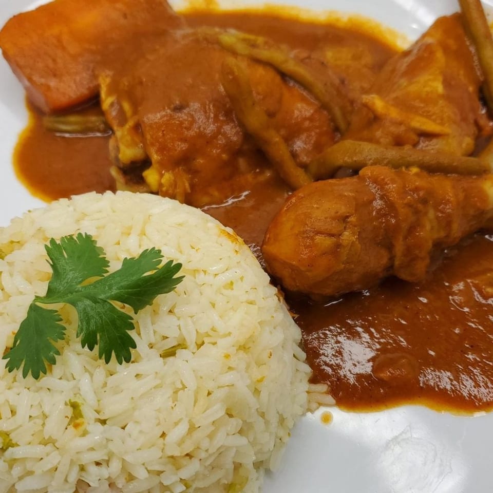 Chicken leg and thigh in a rich orange sauce with rice and cilantro on a white plate.