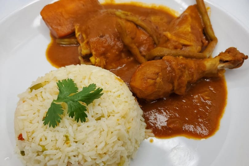 Chicken leg and thigh in a rich orange sauce with rice and cilantro on a white plate.