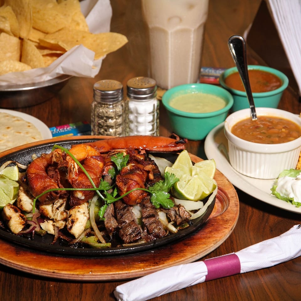 Sizzling fajitas with shrimp, steak, chicken, and vegetables, served with rice, beans, and tortillas.