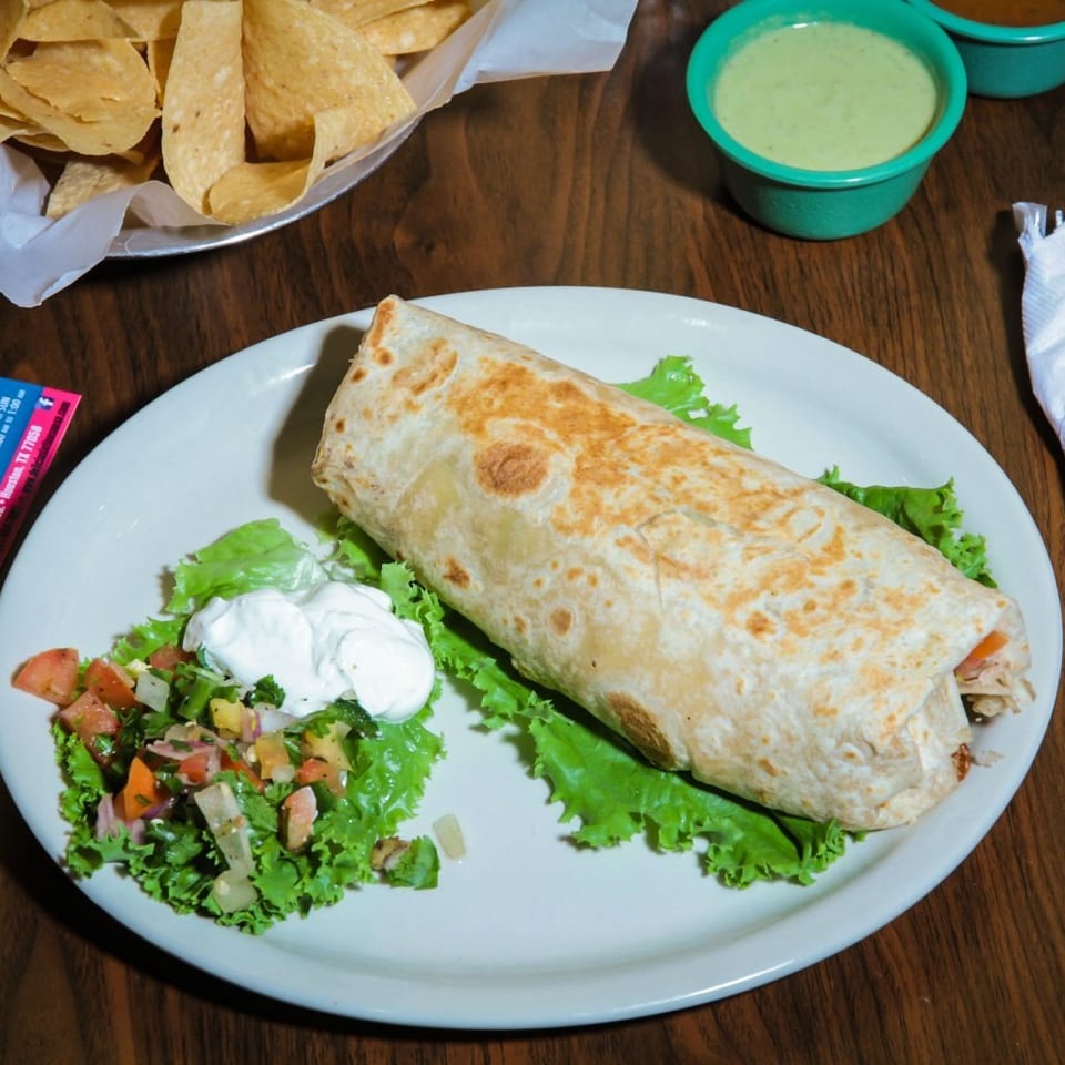 A large burrito with lettuce, pico de gallo, and sour cream, alongside chips and salsa.
