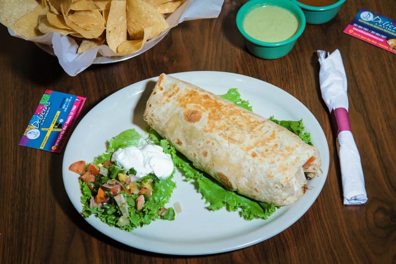 A large burrito with lettuce, pico de gallo, and sour cream, alongside chips and salsa.
