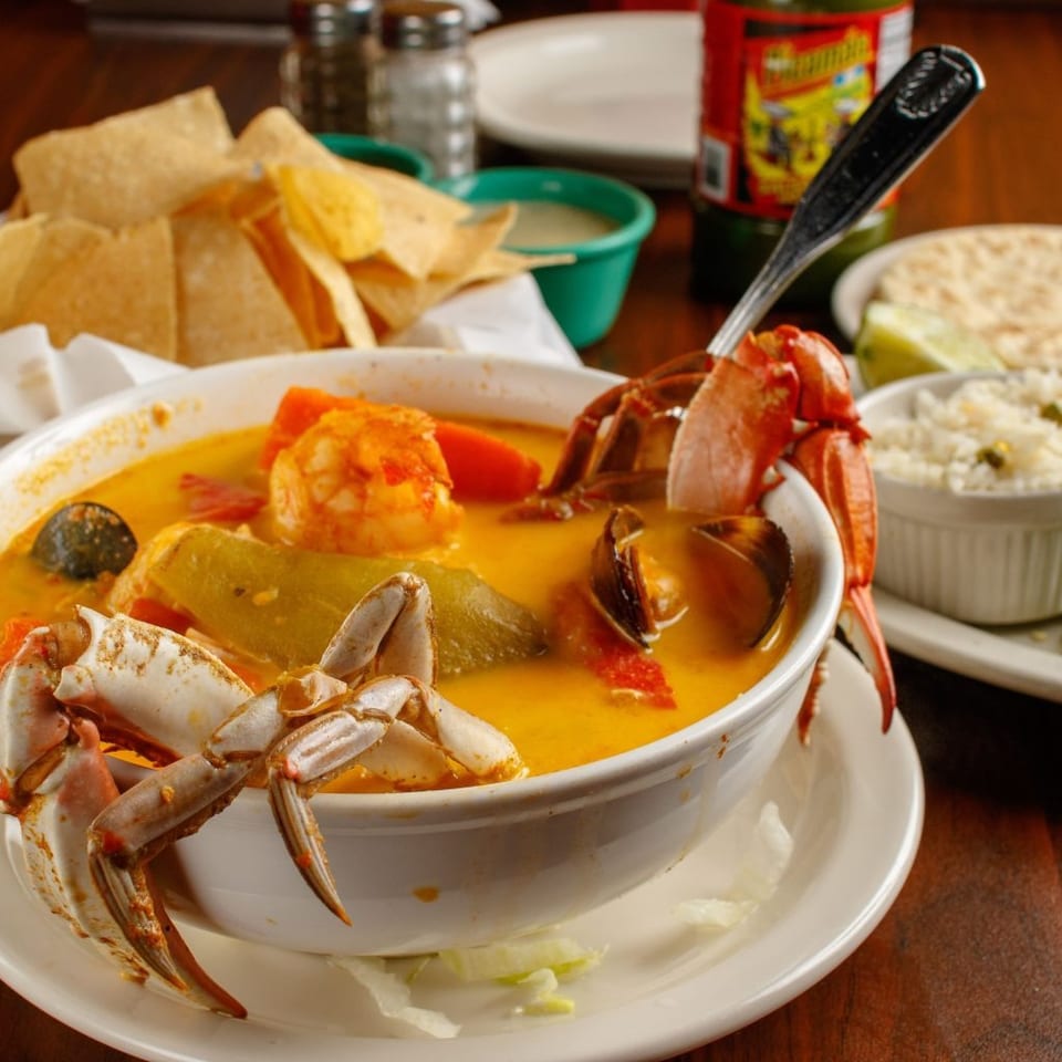 Seafood soup with crab, shrimp, and vegetables, served with tortilla chips, rice, and tortillas.