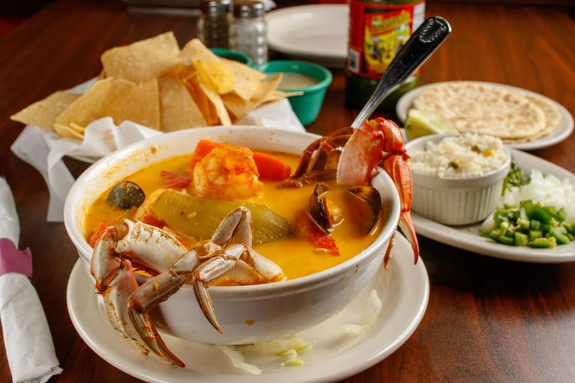 Seafood soup with crab, shrimp, and vegetables, served with tortilla chips, rice, and tortillas.